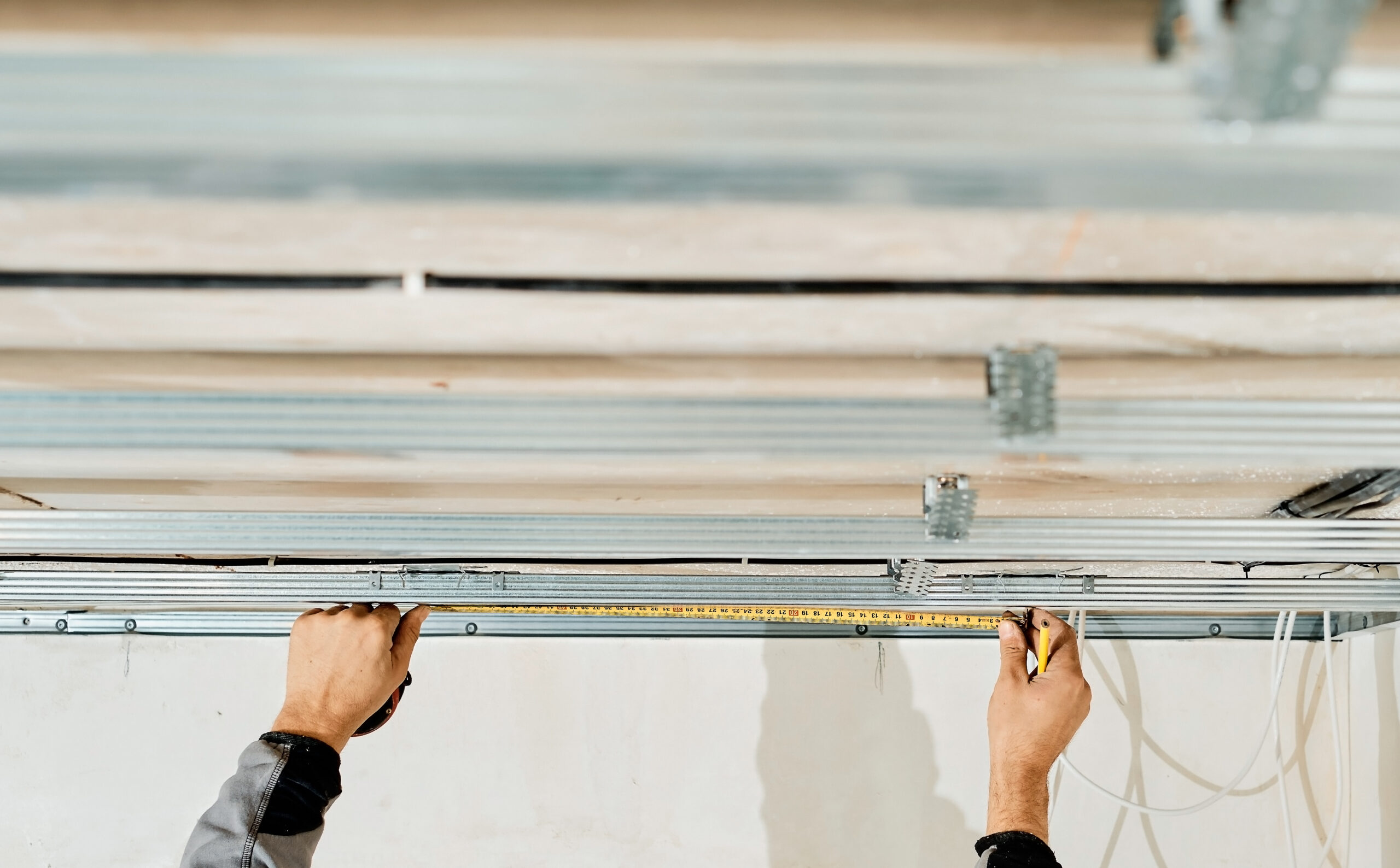 Worker's hands measure and adjust a metal profile for mounting a plasterboard ceiling frame, close-up, selective focus in the hands of a specialist. Industrial renovation and renovation